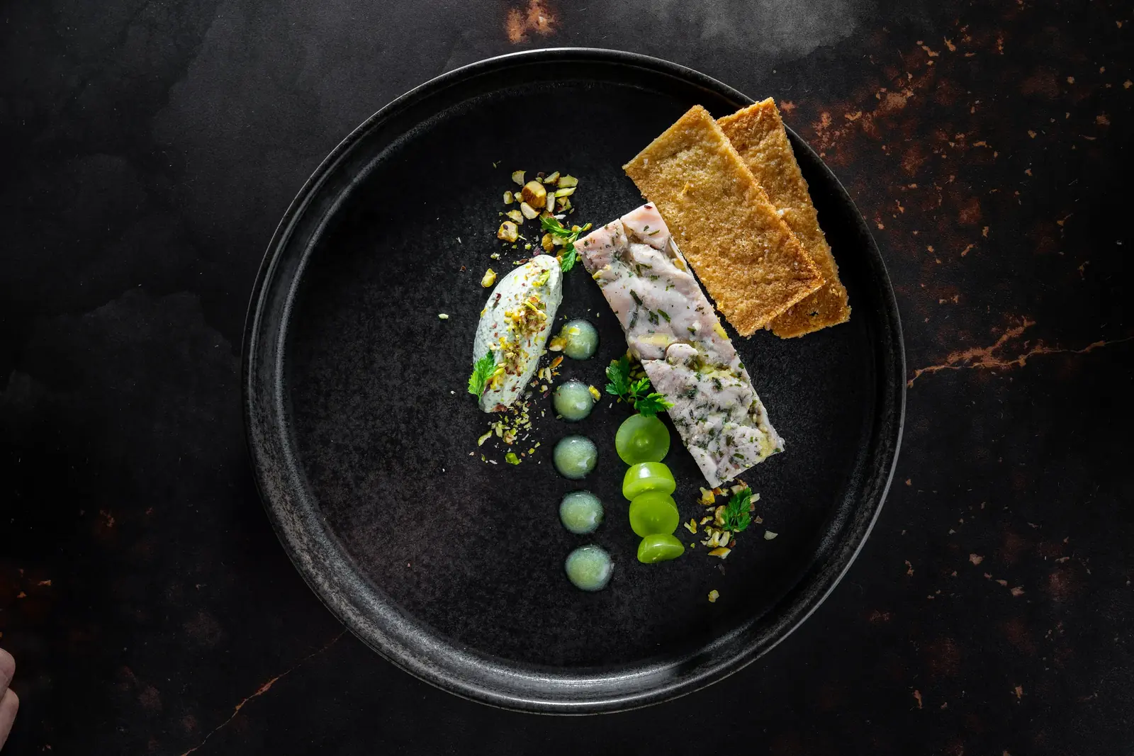 Plated starter of pressed terrine, green spheres and toasted crisps on a black plate, fine dining at home in Cape Town by myCHEF Cape Town